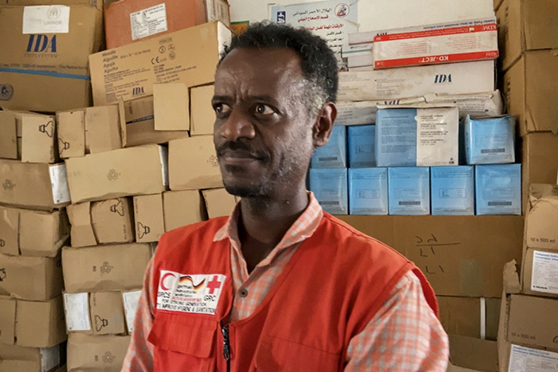 Ethiopian refugee doctor with boxes of supplies in background.