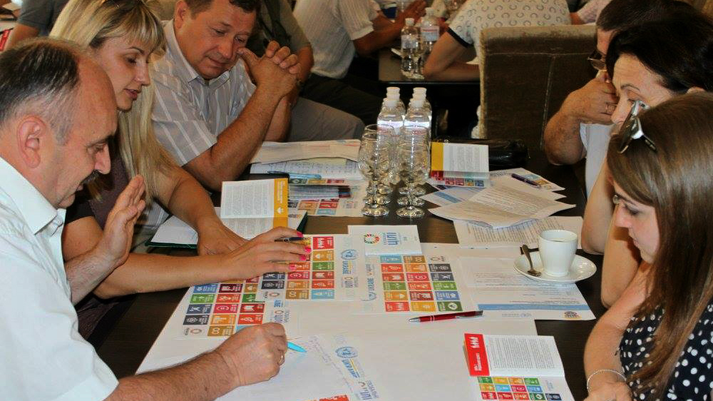 Personas sentadas alrededor de una mesa leyendo folletos de los Objetivos de Desarrollo Sostenible