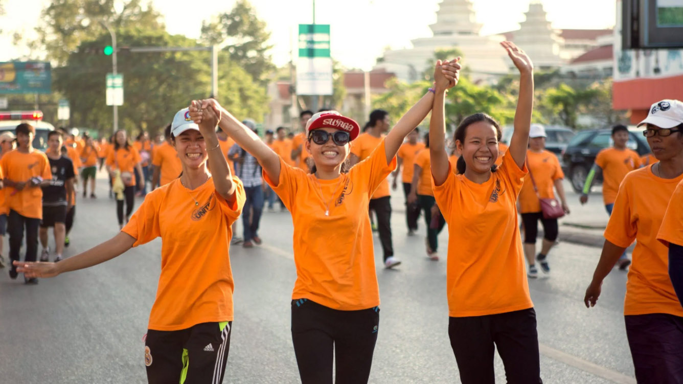 Trois filles en t-shirt orange marchent parmi une foule de personnes habilles en orange.