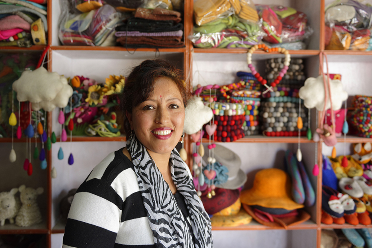 A woman stands in front of the stands full of product at her shop.