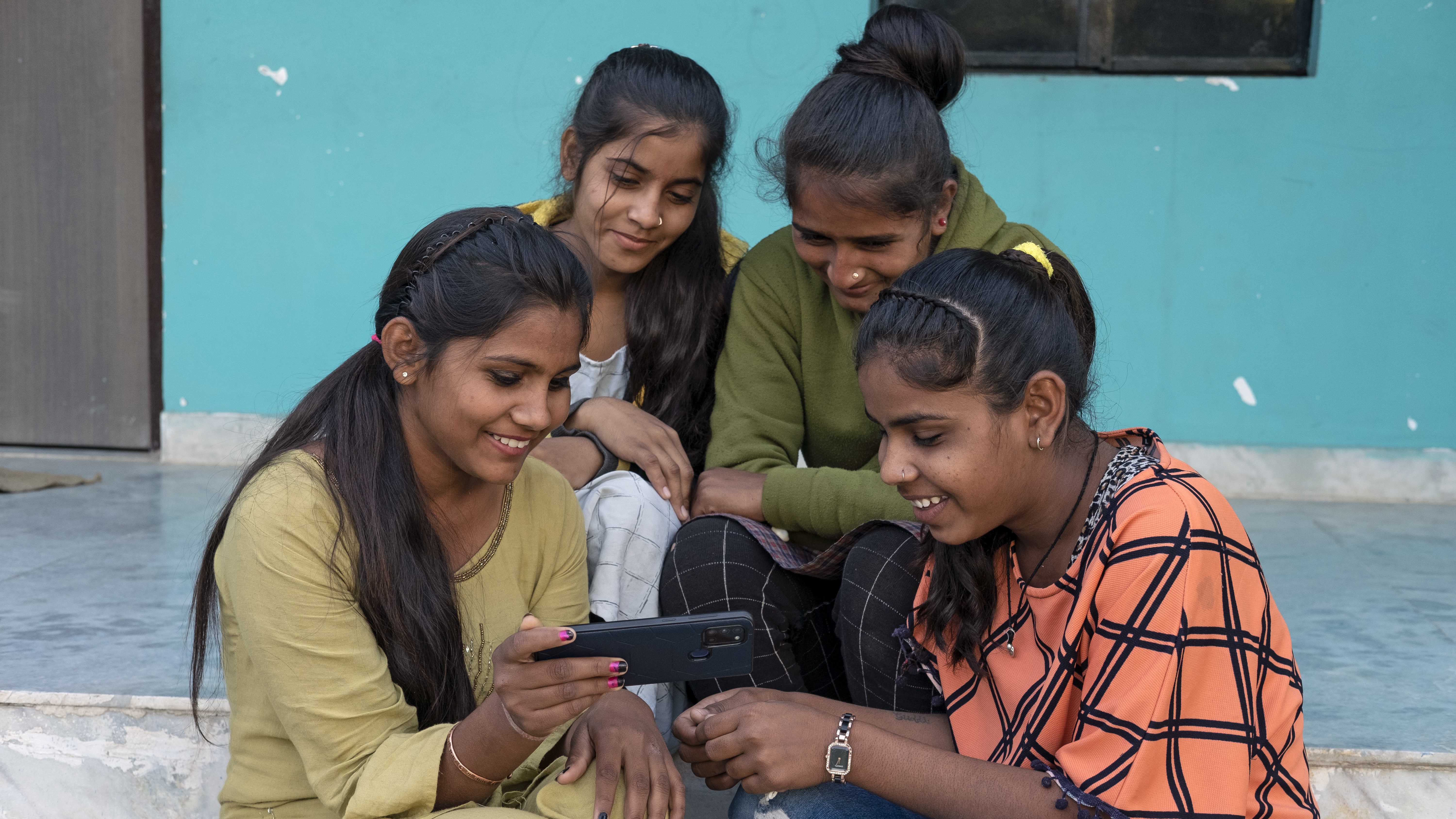 Un groupe d'adolescentes assises sur des marches regarde l'cran d'un tlphone portable.