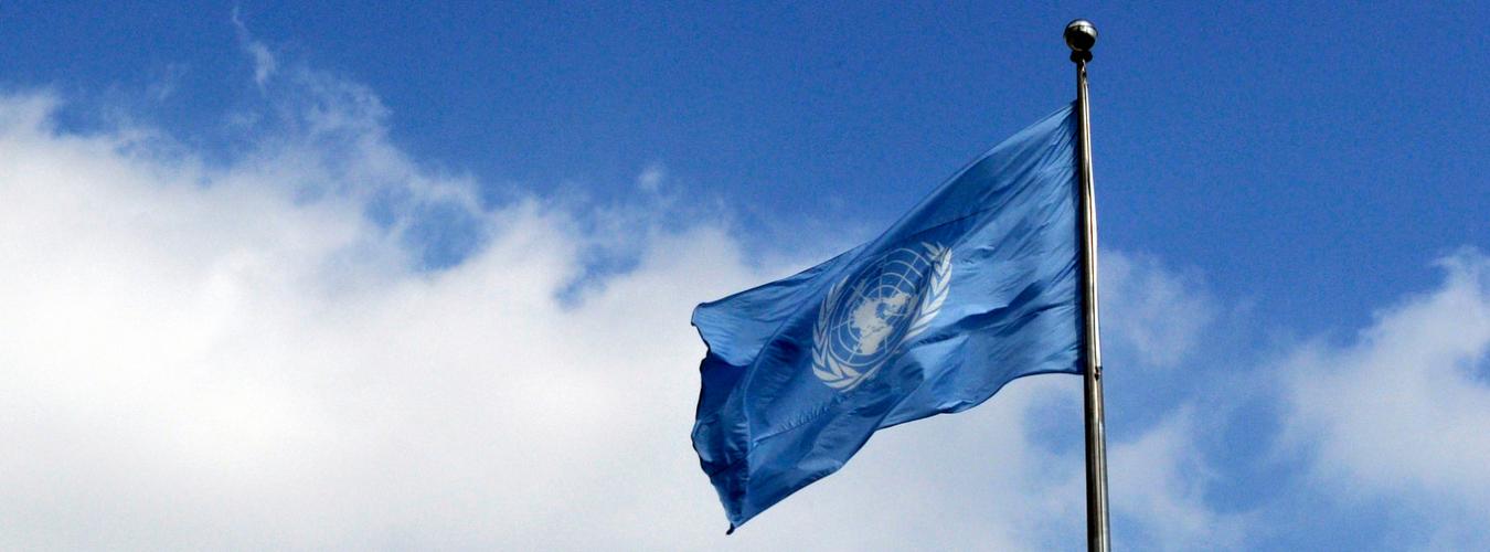 Gros plan sur le drapeau des Nations Unies flottant contre un ciel bleu.